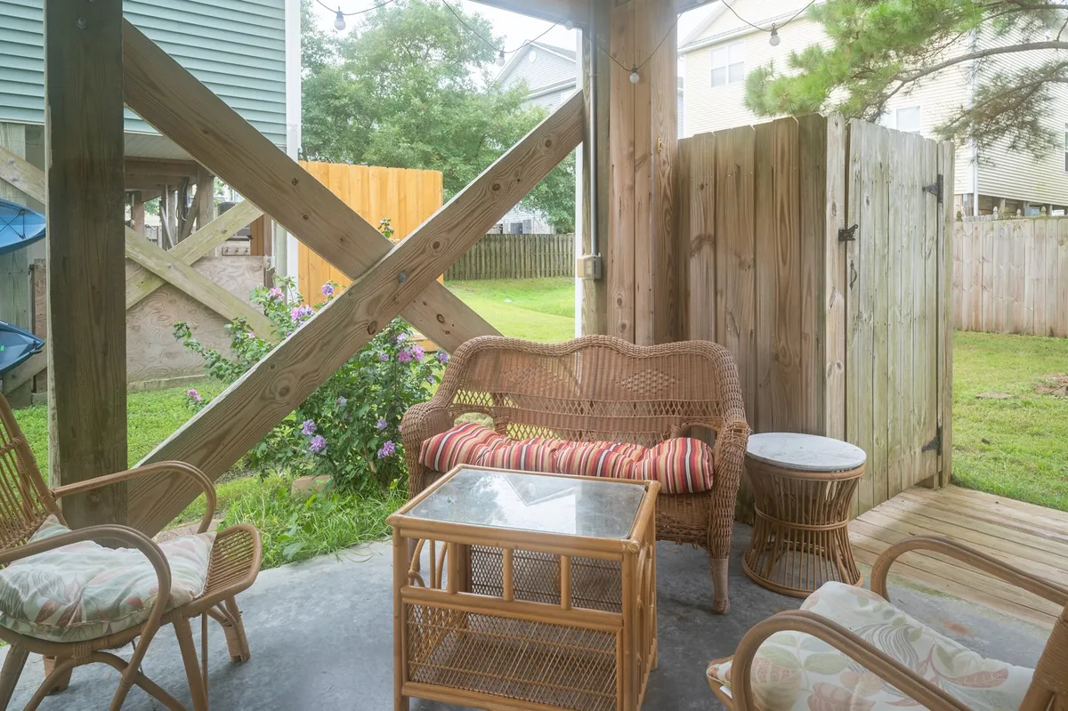 A cozy outdoor seating arrangement with wicker chairs and a glass top table is set amid green foliage and bordered by a wooden fence. The space feels both private and playful, ideal for families or pets to enjoy the yard.