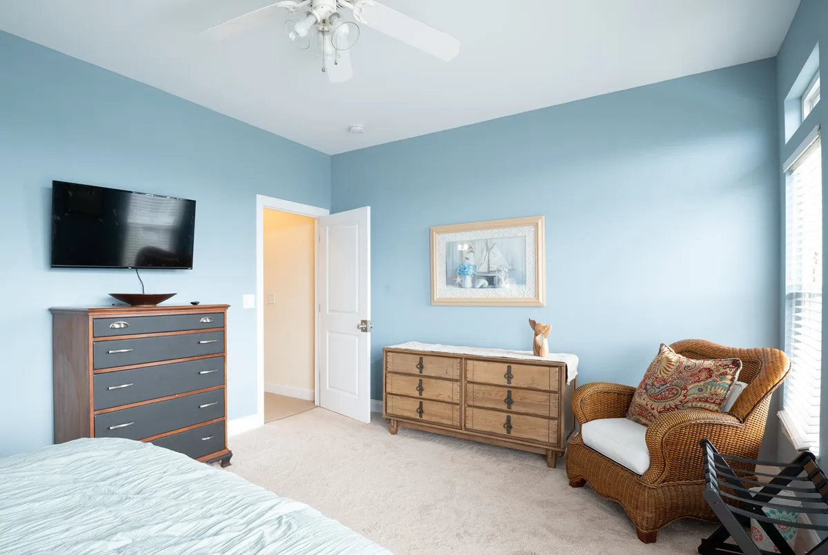 A serene bedroom scene with blue walls, a dresser, a TV, and a wicker chair. The tranquil mood and natural light evoke a restful retreat after a day of local adventures.