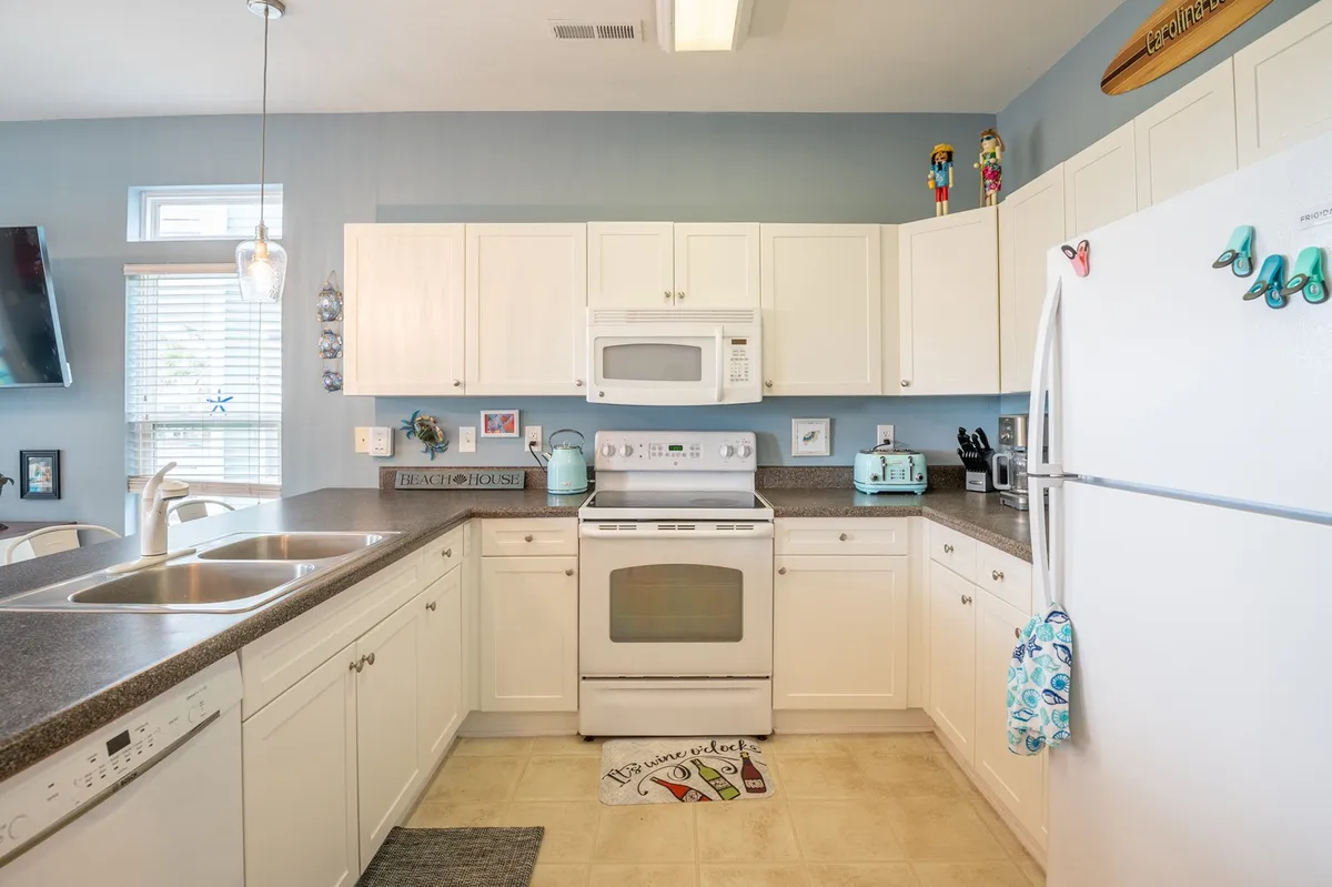 A bright and airy kitchen with white cabinetry, granite countertops, light blue walls, and pastel-colored appliances. Decorative beach-themed items add a playful touch, making it an inviting hub for family cooking and meals.