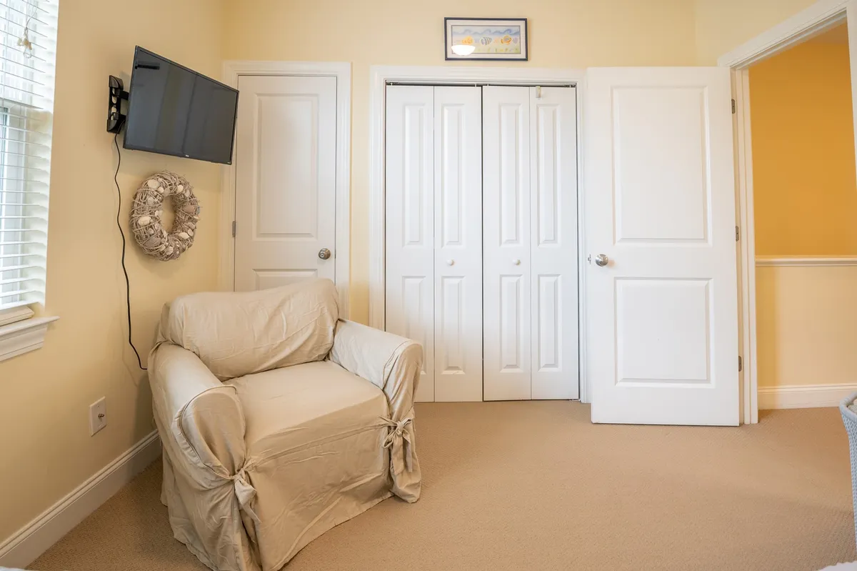 A comfortable living area with a cozy chair, television, and double doors that likely lead to an outside space. The decor is warm and inviting, with touches like a decorative wreath enhancing the welcoming feel.