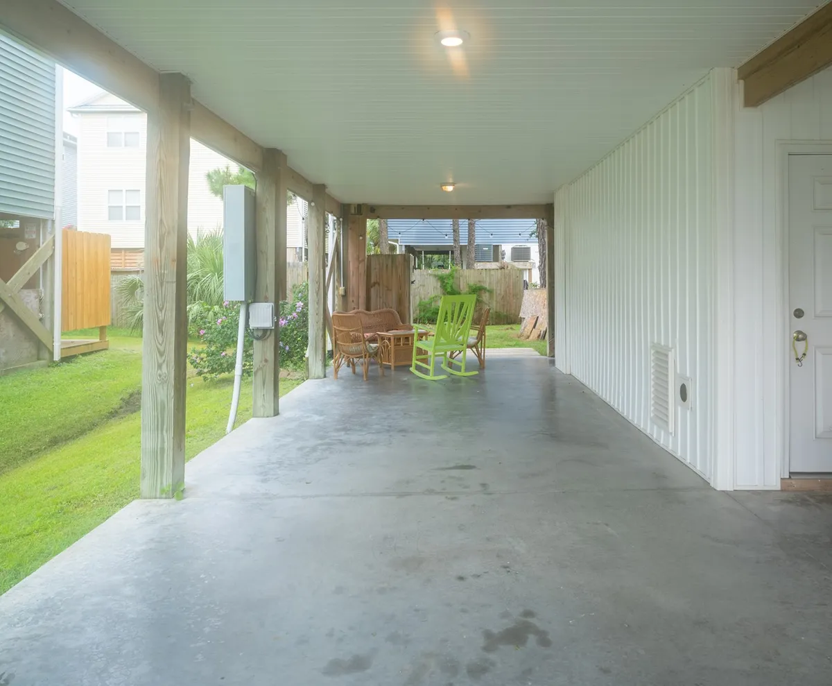 A welcoming, casual seating area with a green rocking chair and woven seats, set on a concrete floor. The space suggests an outdoor or transitional area perfect for relaxing with friends and family, enjoying morning coffee, or gathering after a day at the beach.